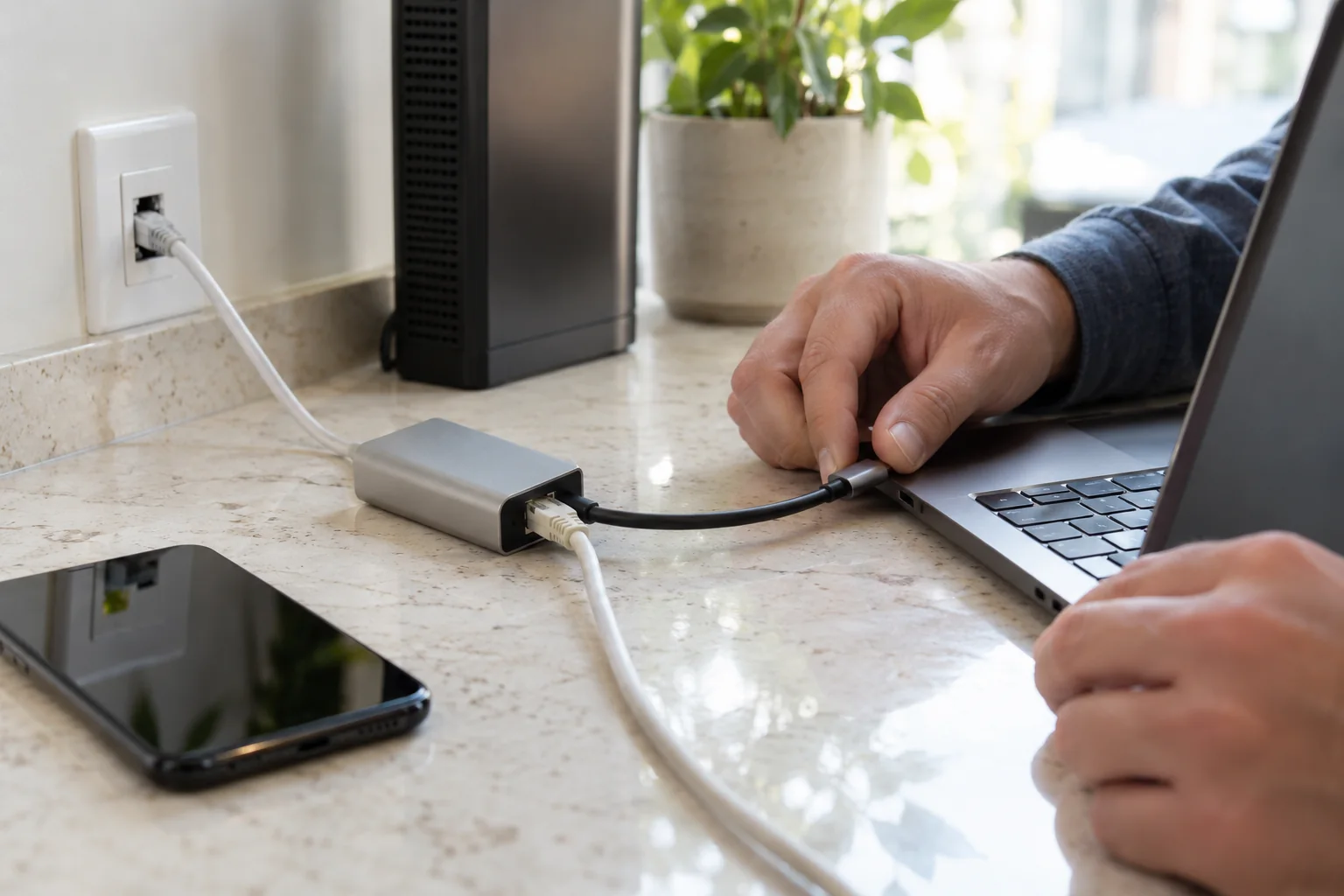 手部在石材工作区连接笔记本与USB-C网络扩展坞，旁边可见手机和家庭网关